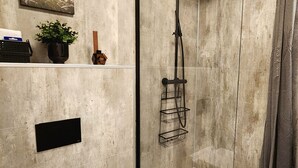 A modern bathroom with a glass-enclosed shower, a white toilet, and a shelf with toiletries. - Base apartments Iceland - cozy studio apartment - capital area (Hafnarfjörður)