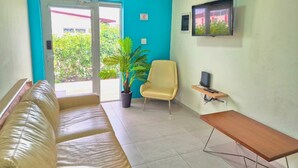 A room with a sofa, a chair, a small table, a potted plant, and a TV mounted on the wall. - Ocean Breeze Apt #2 - 1BR 2Beds with pool (Oranjestad)