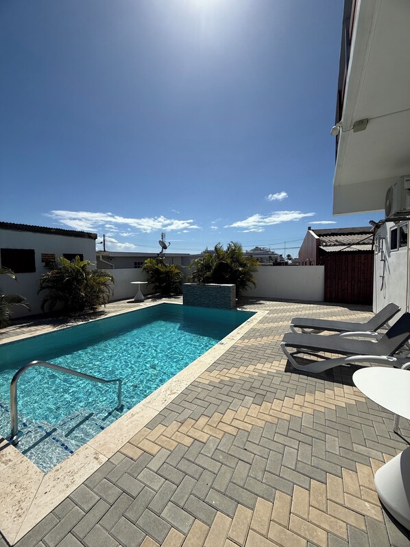 A swimming pool with a tiled deck, lounge chairs, and a clear blue sky.