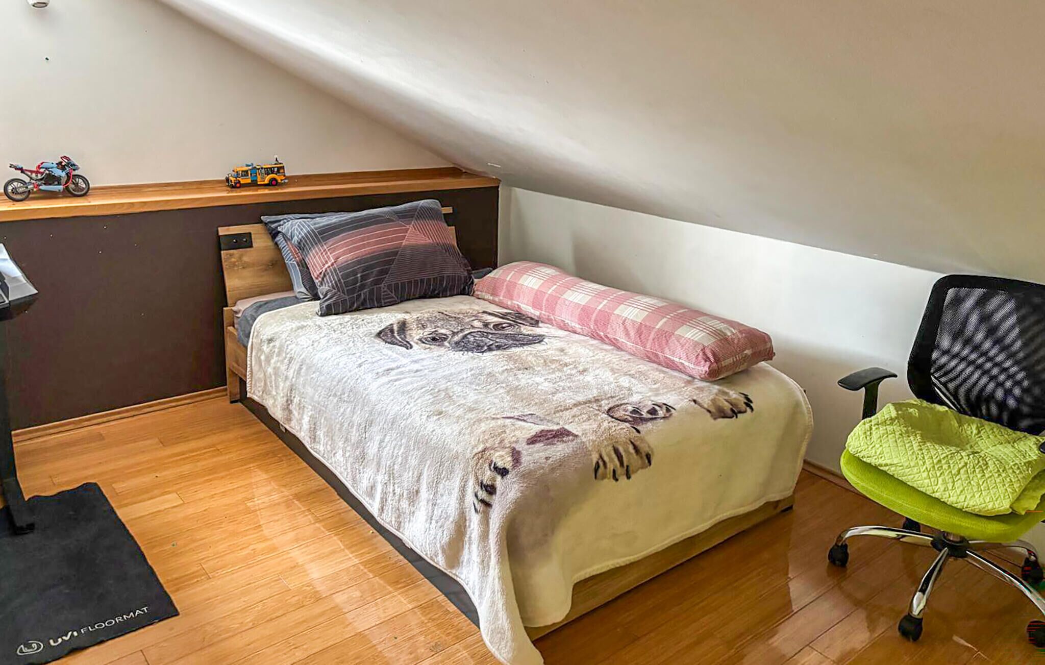 A bedroom with a bed, pillows, a chair, and a small table with toys.