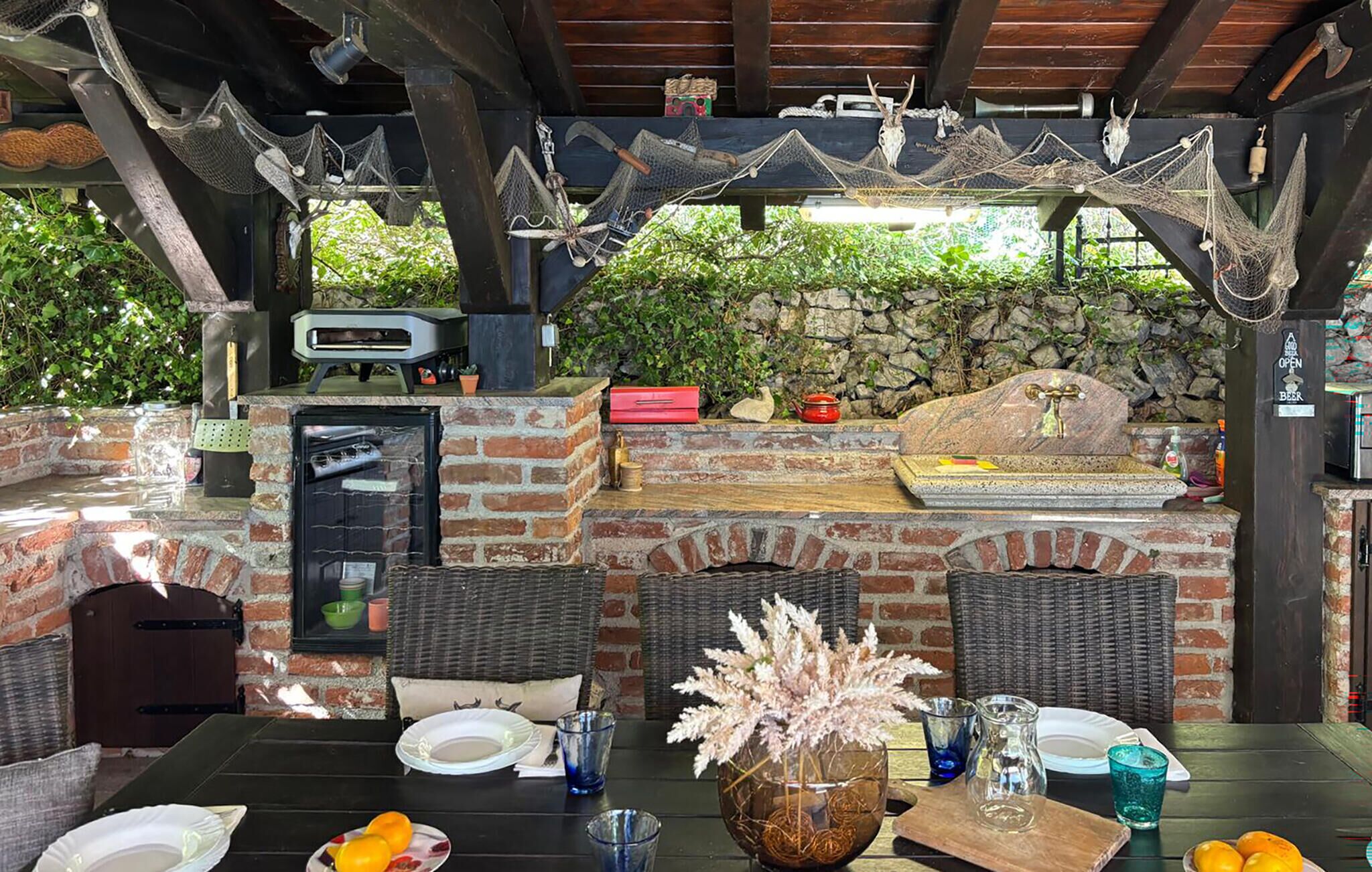 Une terrasse extérieure avec un barbecue en briques, des meubles en osier et un mur en pierre en arrière-plan.