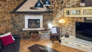 A cozy living room with a stone wall, a fireplace, a leather sofa, a coffee table, a TV, and a lamp. - 3 bedroom gorgeous home in Krasica (Krasica)