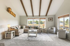 Un salon comprenant un canapé, une table basse et un fauteuil. Il y a des fenêtres donnant sur l’extérieur.