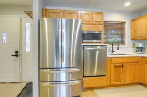 A modern kitchen with stainless steel appliances, wooden cabinets, and a window with blinds.