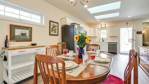 A dining area with a wooden table set for four, surrounded by chairs. A white cabinet with a shelf is to the left, and a refrigerator is in the background. - Walk to Historic Chestertown: Dog-Friendly Retreat (Chestertown)