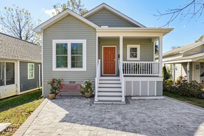 A two-story house with a front porch, a brown door, and a small garden area with potted plants.