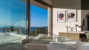 Quarto de hotel com uma grande janela com vista panorâmica, cama com toalhas bem organizadas e duas obras de arte emolduradas na parede.