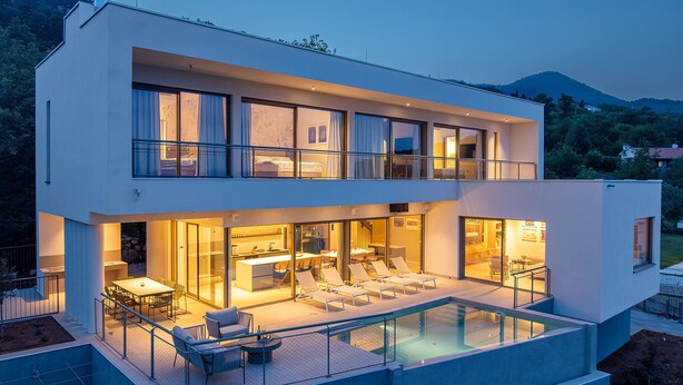 Uma casa moderna de dois andares com piscina envidraçada, área de estar externa e espaço para refeições.