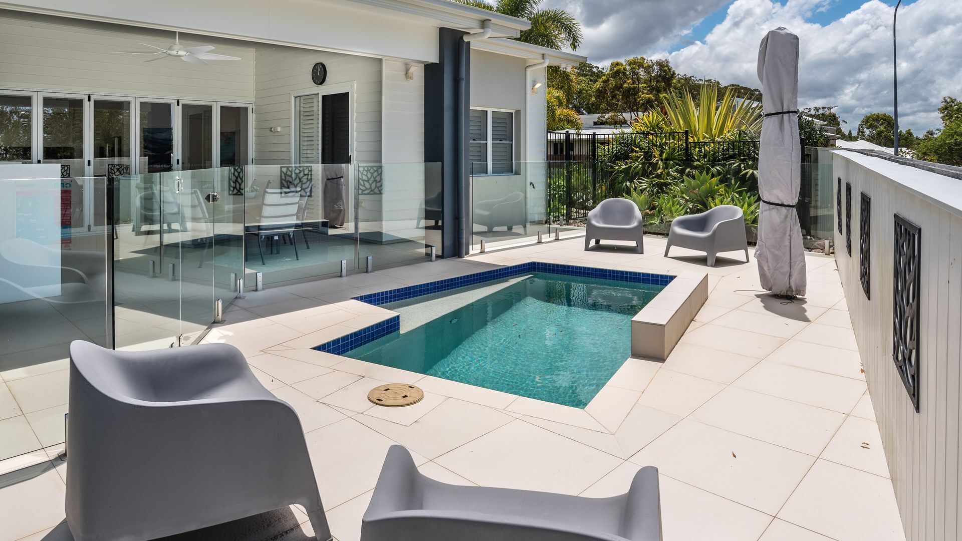 A modern outdoor pool area with a glass-enclosed pool, white lounge chairs, and a glass balustrade.