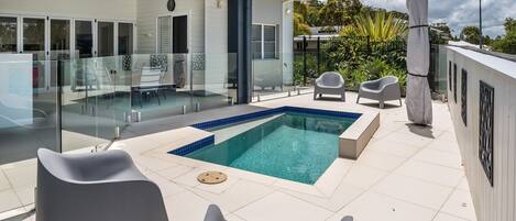 A modern outdoor pool area with a glass-enclosed pool, white lounge chairs, and a glass balustrade.