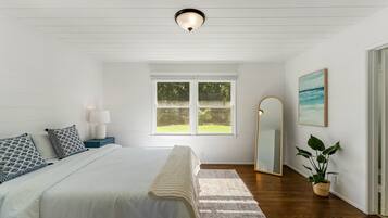 Une chambre à coucher avec un lit, une table de chevet, une lampe, une fenêtre, un miroir et une plante en pot.