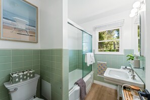 Une salle de bain avec une douche à parois de verre, un lavabo blanc et une fenêtre donnant sur les arbres.