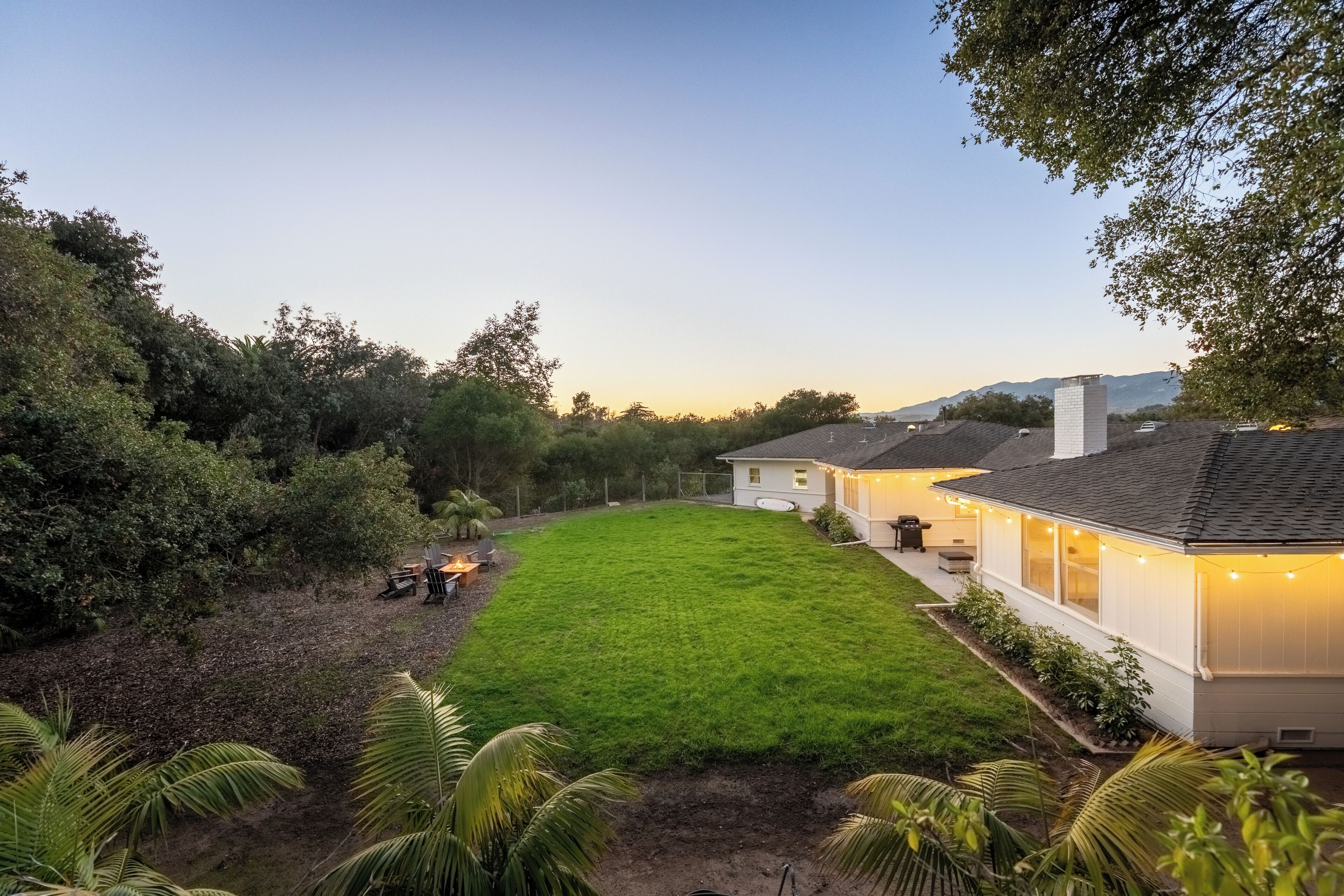 A residential property with a well-maintained lawn, a house with a chimney, and a fenced yard.