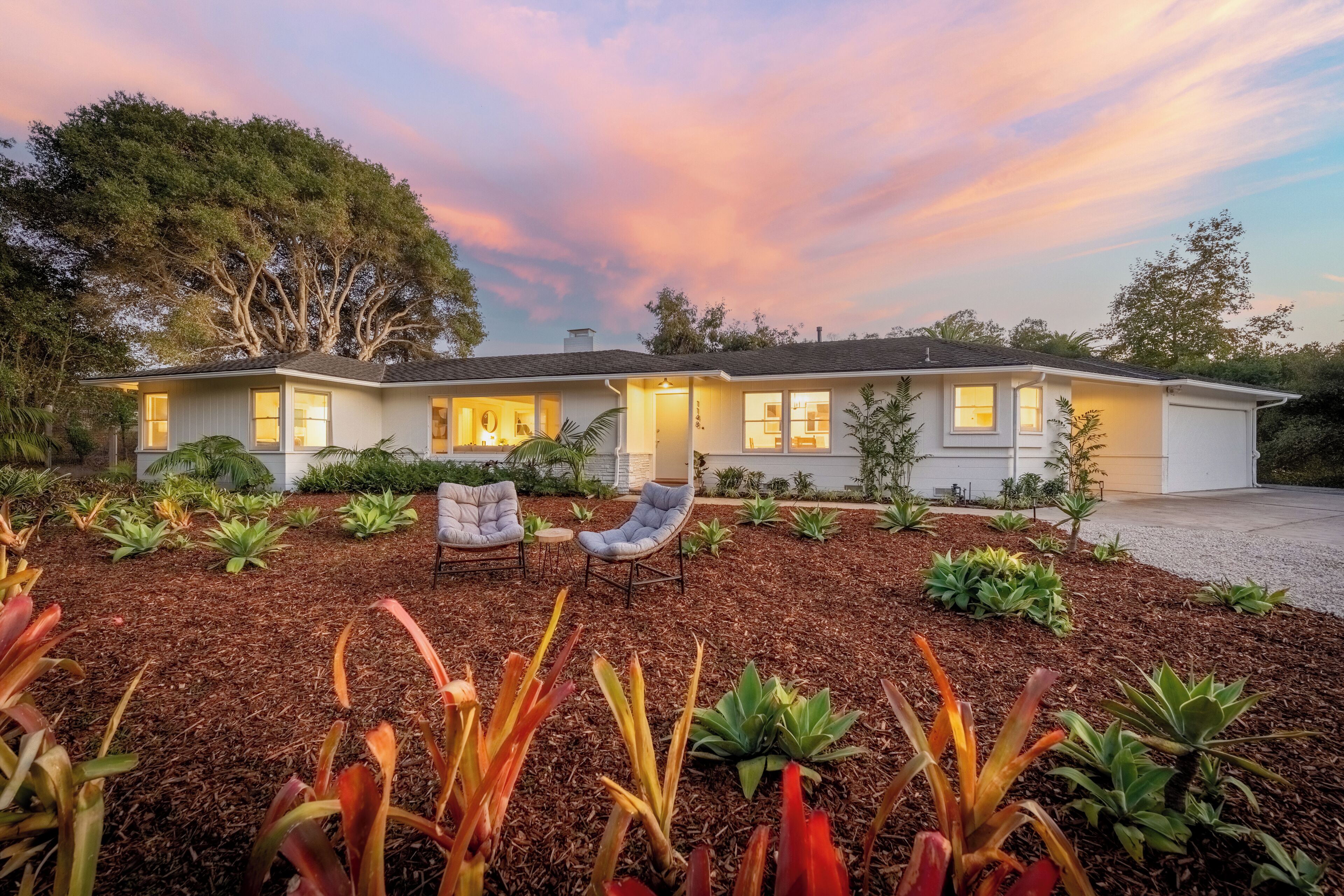 A two-story house with a driveway, outdoor seating, and a garden.