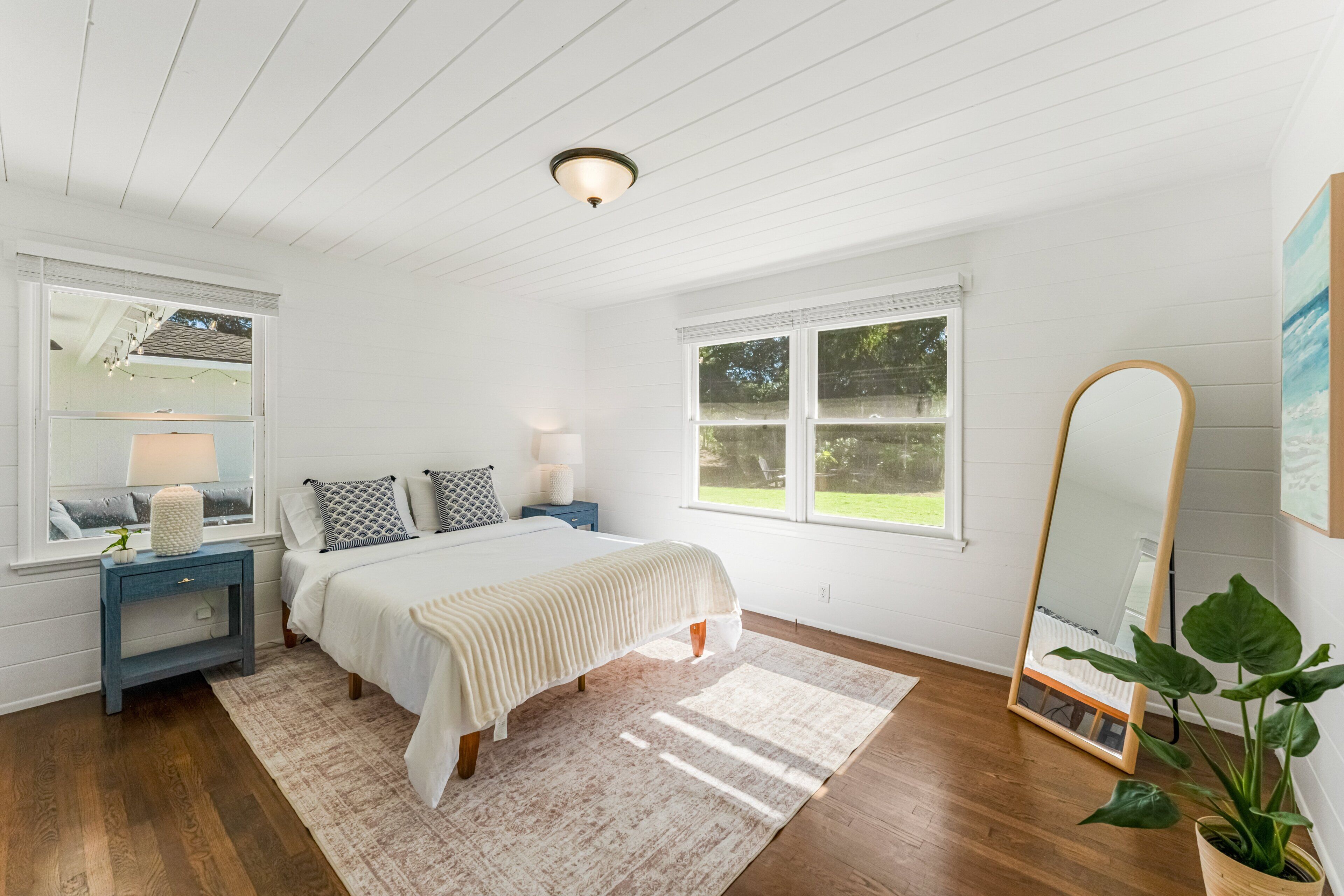 A bedroom with a bed, bedside tables, a mirror, and a window.