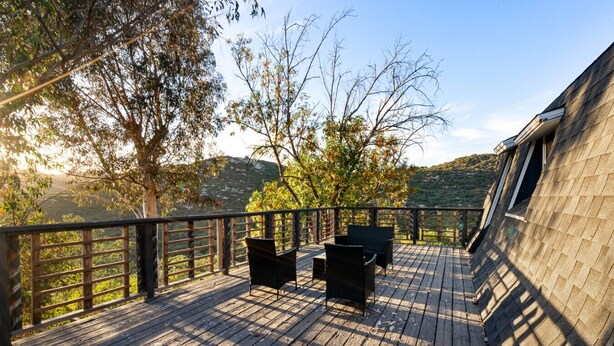 Una terraza de madera con mobiliario exterior, barandilla y vistas a un paisaje montañoso.