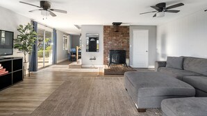 Una sala de estar moderna con chimenea, sofá gris, piso de madera y ventiladores de techo.