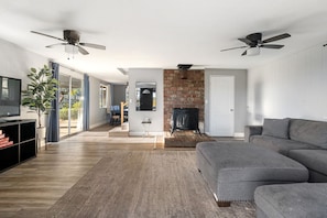 Una sala de estar moderna con chimenea, sofá gris, piso de madera y ventiladores de techo.
