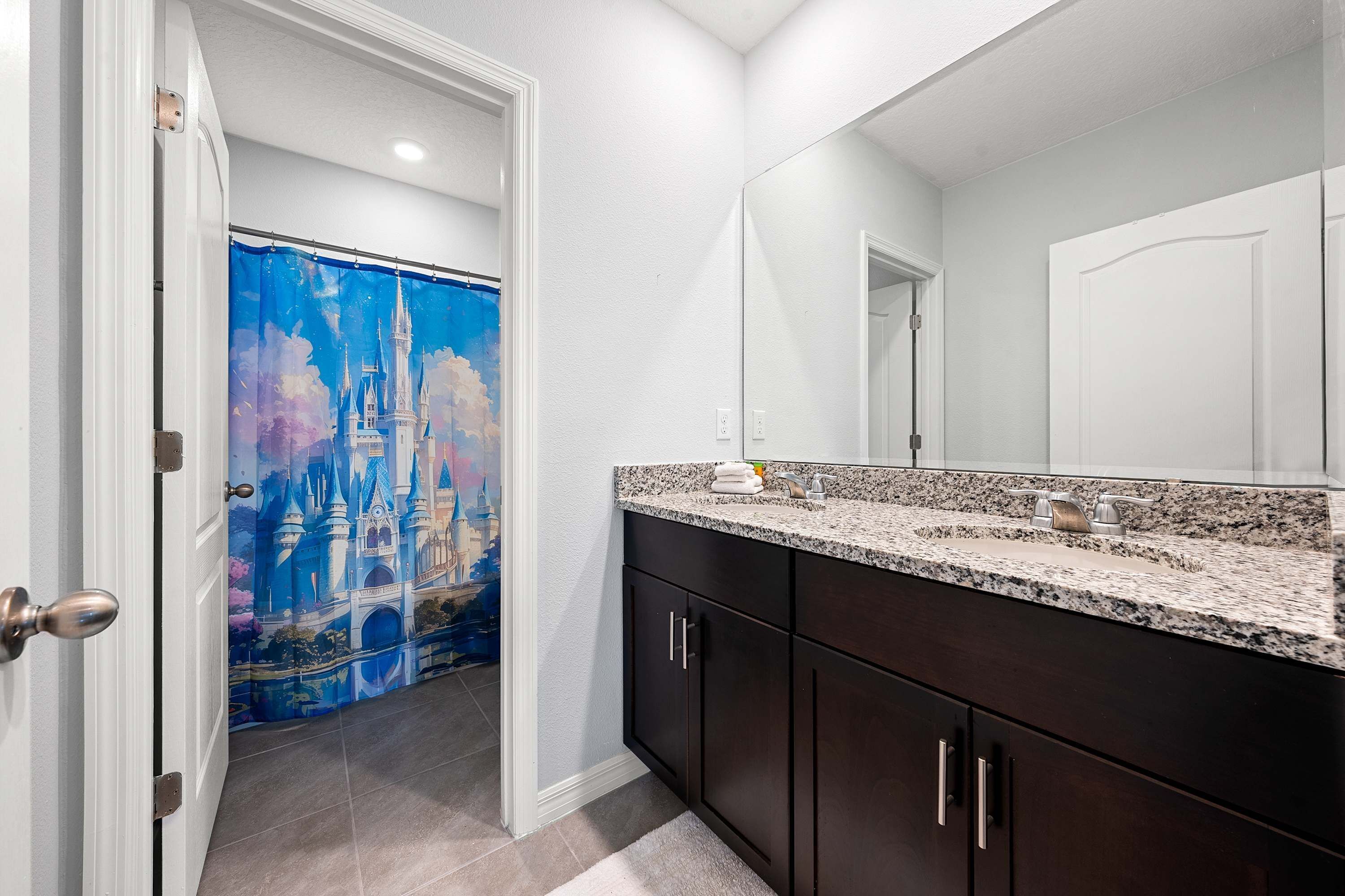 A bathroom with a large mirror, dark cabinets, and a granite countertop.