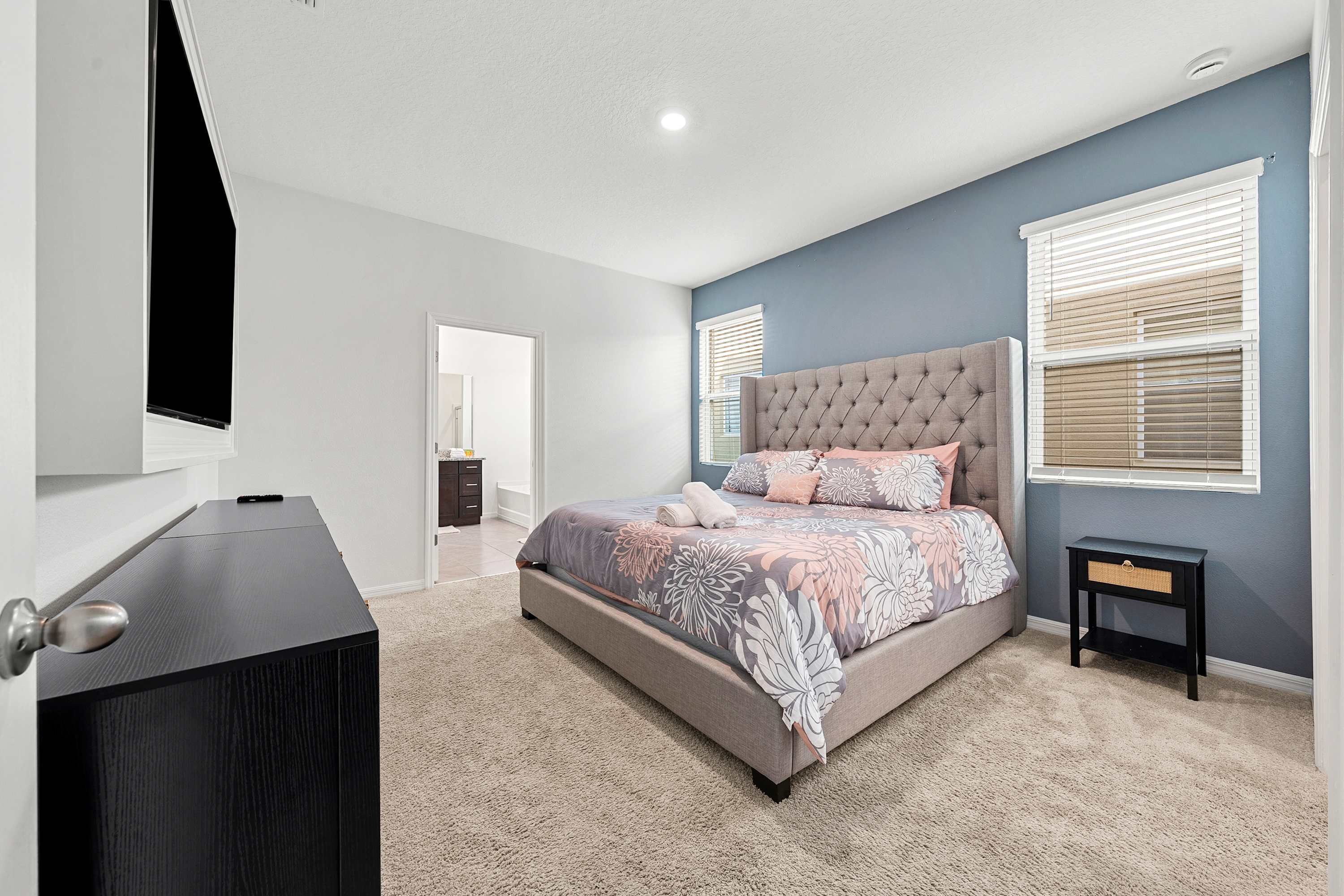 Une chambre à coucher avec un lit, une commode, un téléviseur et une fenêtre avec des stores.