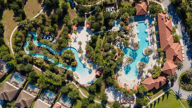 Luchtbeeld van een resort met meerdere zwembaden, palmbomen en een tennisbaan.