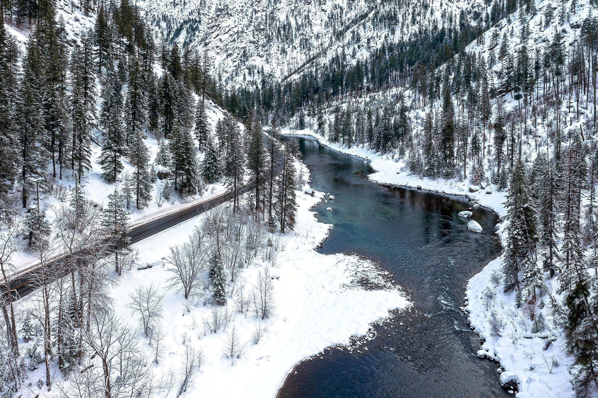 A snow-covered river with a bridge and dense forest.