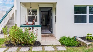 Una casa con fachada blanca, techo verde y un porche con una hamaca.