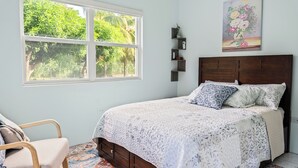 Un dormitorio con cama, una silla, un ventanal y un cuadro en la pared.