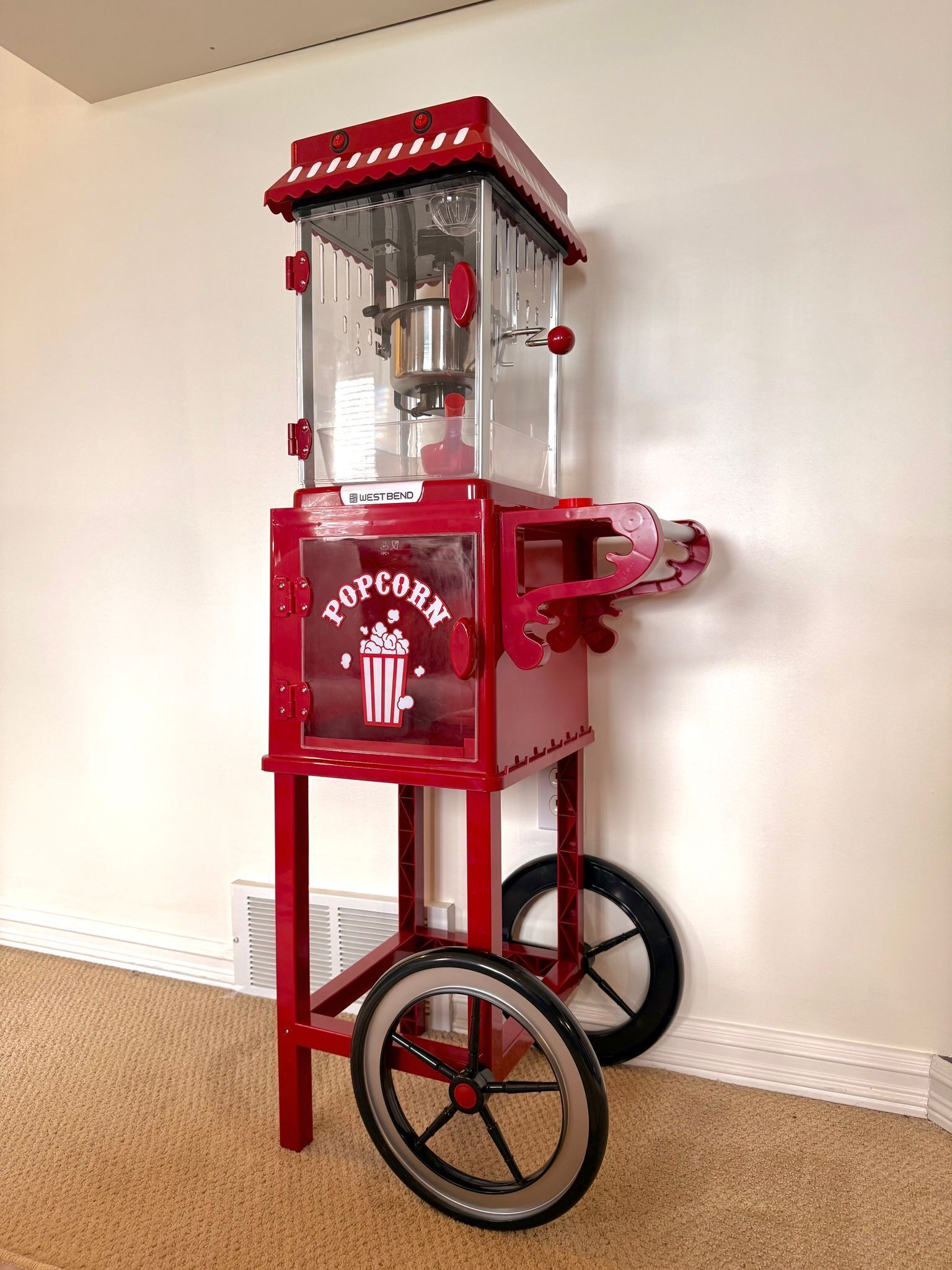 A red popcorn machine with wheels, placed against a wall.