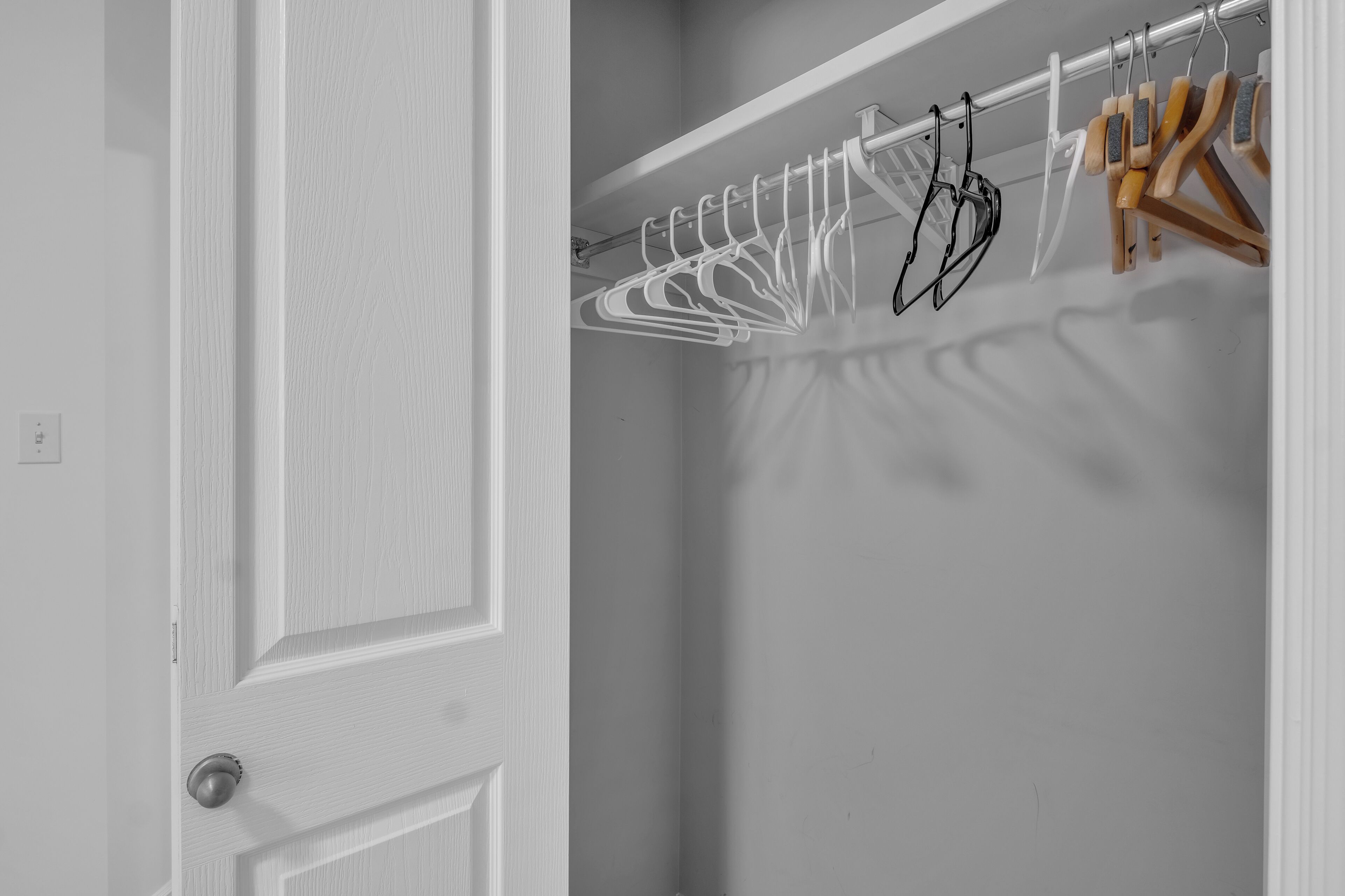 A white door with a silver handle, a white closet with a metal rod holding clothes hangers, and a wooden hanger.
