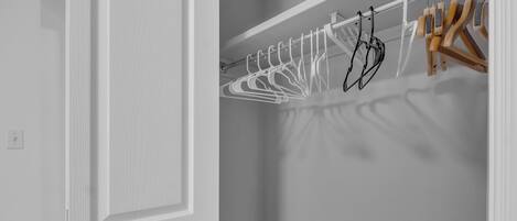 A white door with a silver handle, a white closet with a metal rod holding clothes hangers, and a wooden hanger.