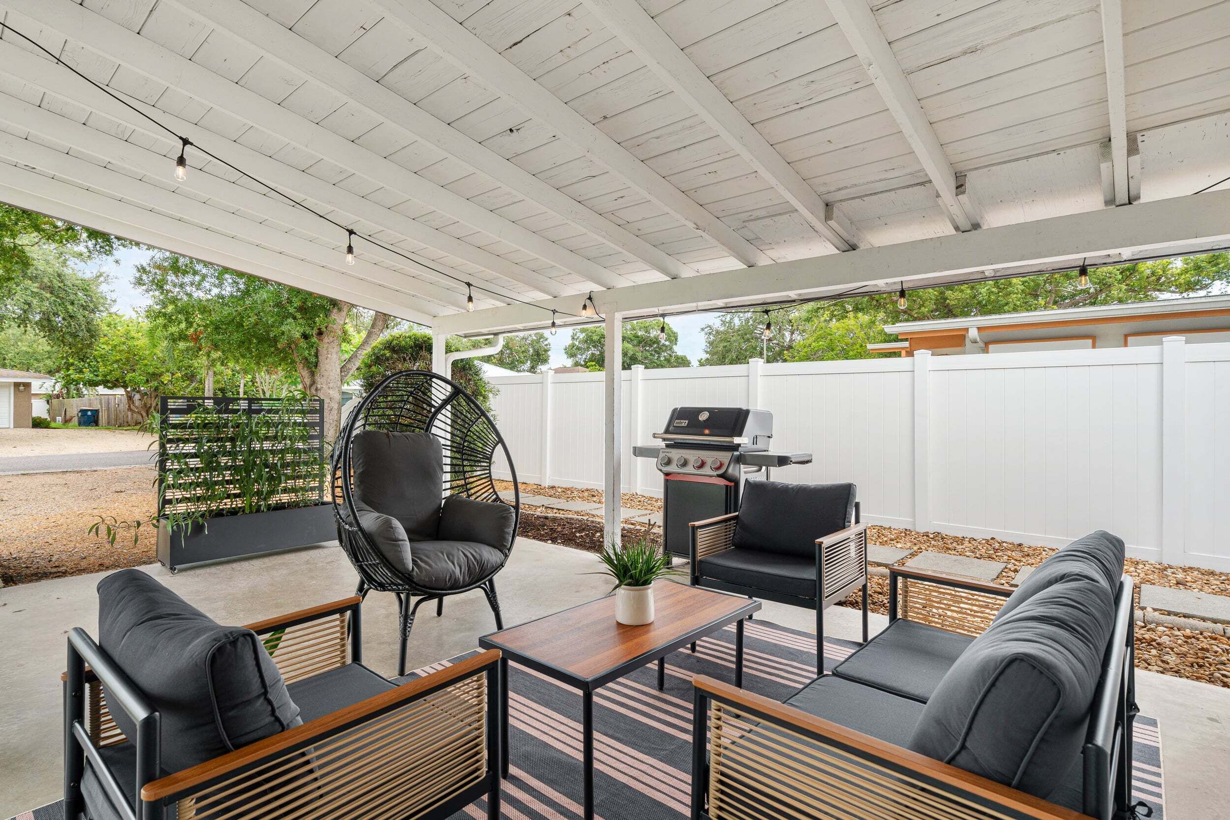 An outdoor patio with a covered seating area, a grill, and a hanging chair.