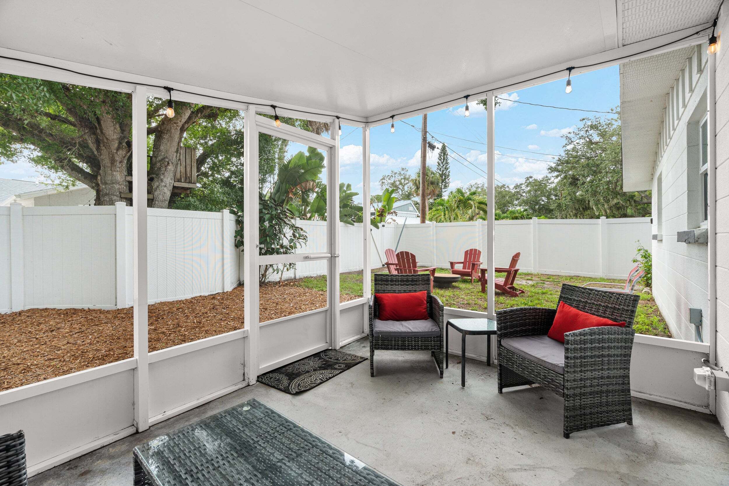 A covered patio area with wicker furniture, a view of the backyard, and a white fence.