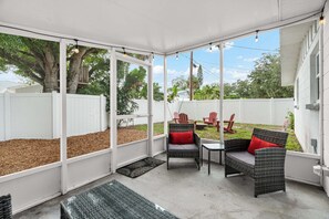 Ein überdachter Patio-Bereich mit Korbmöbeln, Blick auf den Garten und einem weißen Zaun.