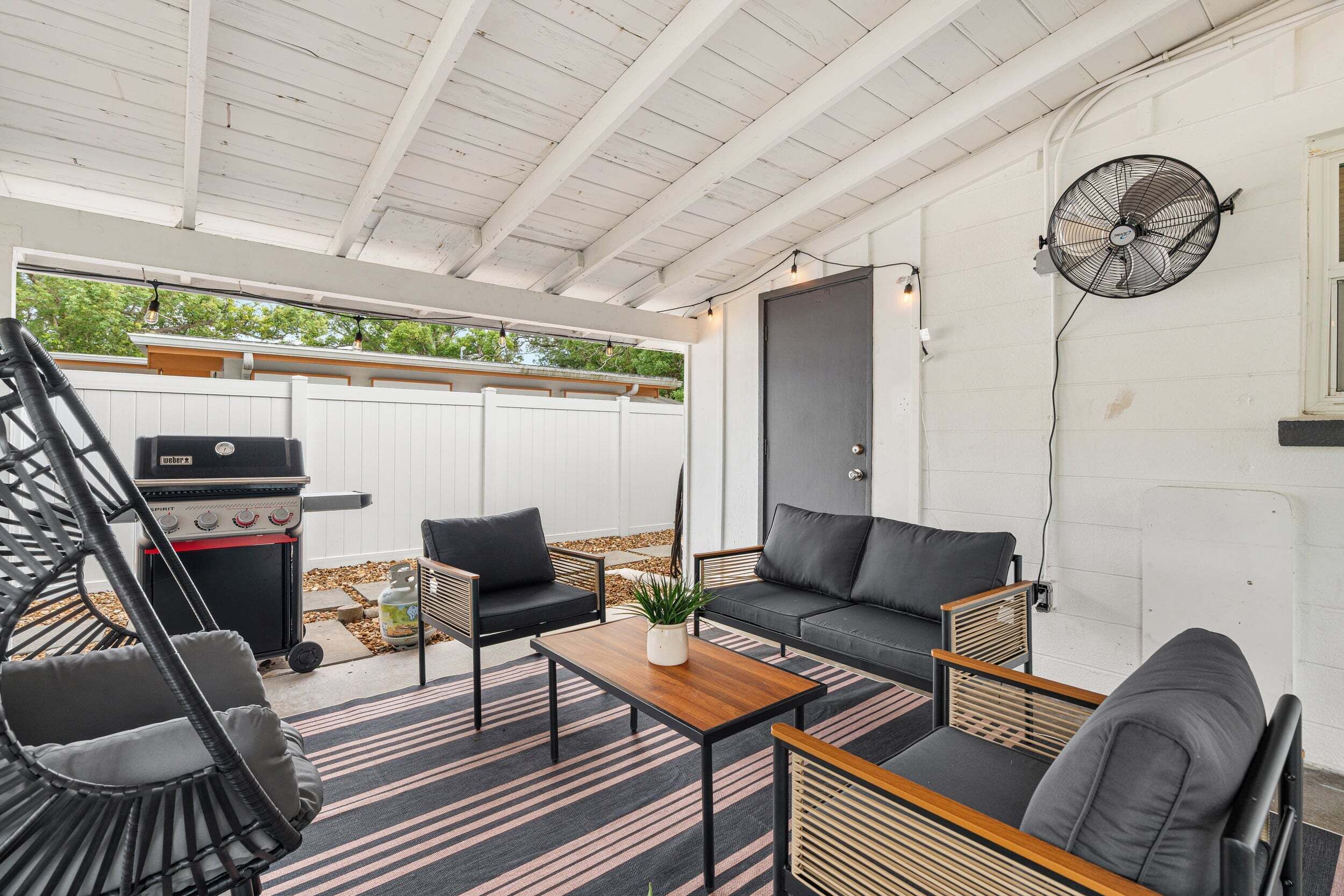 An outdoor patio with a grill, seating, and a fan.