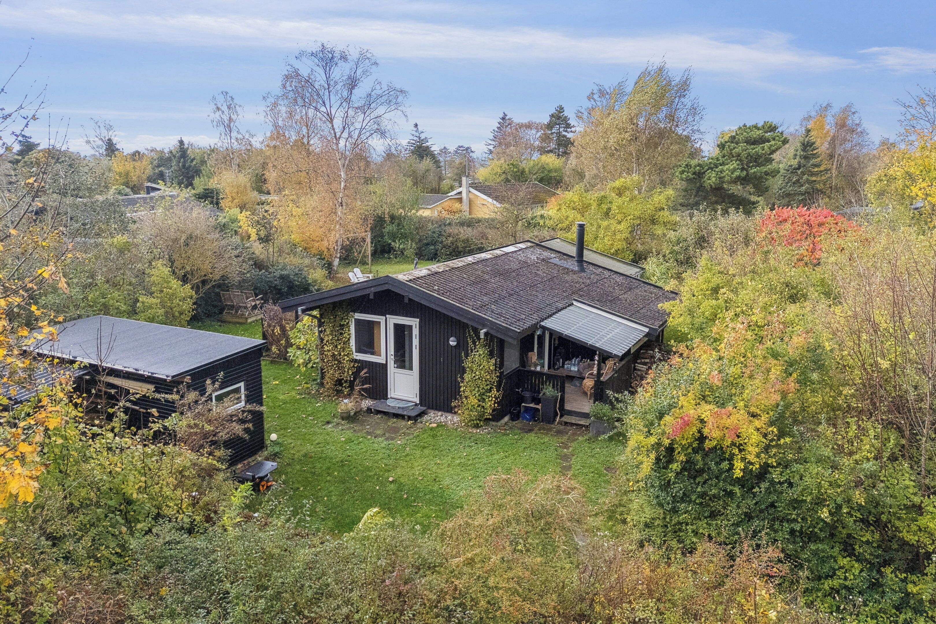 A small house with a sloped roof, a porch, and a yard surrounded by trees.