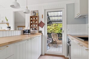 A kitchen with white cabinetry, a wooden countertop, and a view of a balcony with outdoor furniture. - Cozy holiday home by Kelstrup Beach (Slagelse)