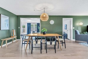 Ein modernes Wohnzimmer mit einem Holzesstisch, schwarzen Stühlen, einer gewebten Pendelleuchte und einem grauen Sofa.