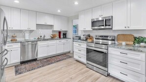 A modern kitchen with white cabinets, stainless steel appliances, and a wooden countertop. - Olive Tree Oasis | 4/2 w/ Hot Tub + Heated Pool (Sarasota)