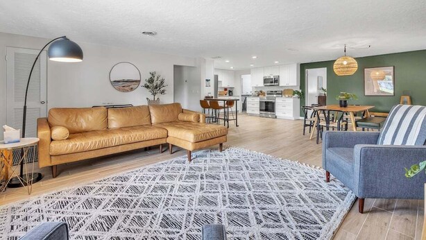 A modern living room with a leather sofa, a patterned rug, and a dining area with a table and chairs. - Olive Tree Oasis | 4/2 w/ Hot Tub + Heated Pool (Sarasota)