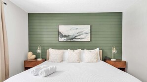 A neatly made bed with white bedding, two bedside tables with lamps, and a green wall with a framed picture above the bed. - Olive Tree Oasis | 4/2 w/ Hot Tub + Heated Pool (Sarasota)
