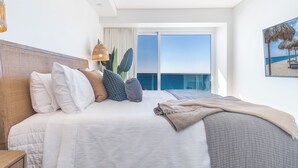Ein modernes Hotelzimmer mit einem großen Bett, Meerblick und einem Balkon mit Stadtpanorama im Hintergrund.