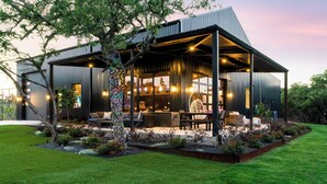 A modern house with a covered outdoor area, a lawn, and a tree. - NEW Luxe Estate, Pond, Pool, Pickleball, Animals, 20 PPL (Dripping Springs)