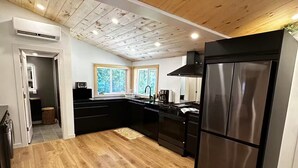 Eine moderne Küche mit Holzböden, einem schwarzen Kühlschrank und einem großen Fenster, das für natürliches Licht sorgt.