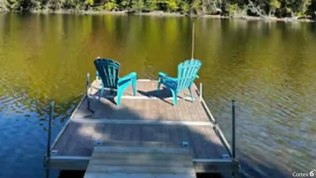 Eine Holzsteg mit zwei türkisblauen Adirondack-Stühlen, die auf einen ruhigen See mit dichter Ufervegetation blicken.