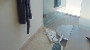A bathroom with a glass door leading to a balcony, a towel rack with a robe, and a bench.