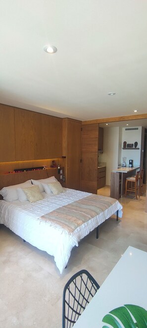 Une chambre dotée d’un grand lit, d’une tête de lit en bois, d’une armoire intégrée et d’un petit coin cuisine.