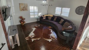 A spacious living area with a curved sectional sofa, a wooden coffee table, and a large cowhide rug. - 511 Western Casa, Where Timeless Western Aesthetics meets Modern Comfort (Marlow)