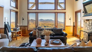 A spacious living room with a large window offering a mountain view, a fireplace, and a cozy seating area. - Over The Top: Custom Luxury Home! Views, Hot Tub, Pool Table, Firepit, Claw Machine, More! (Banner Elk)