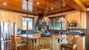 A spacious kitchen with wooden cabinets, stainless steel appliances, and a central island with bar stools. - Over The Top: Custom Luxury Home! Views, Hot Tub, Pool Table, Firepit, Claw Machine, More! (Banner Elk)